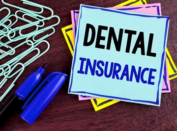 A pile of paper clips, a blue sharpie, and a stack of post-it notes with the top one reading “Dental Insurance”