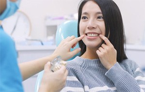 A woman pointing at her smile and listening to a dentist.