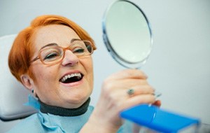 A senior woman admiring her new dentures with a hand mirror