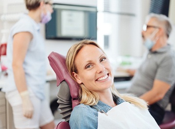 A middle-aged woman smiling in the dentist’s chair while the dentist and dental hygienist talk in the background