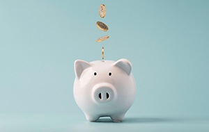 Coins falling into white piggybank against teal background