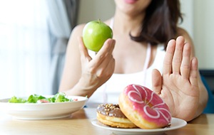 Woman holding an apple and pushing back plate of donuts