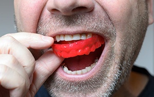 man putting red mouthguard in his mouth 