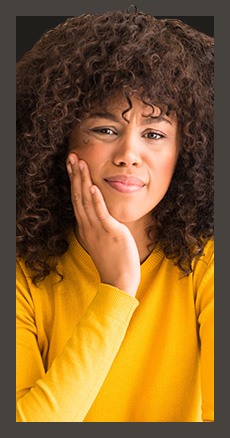 Woman in yellow blouse holding her cheek in pain