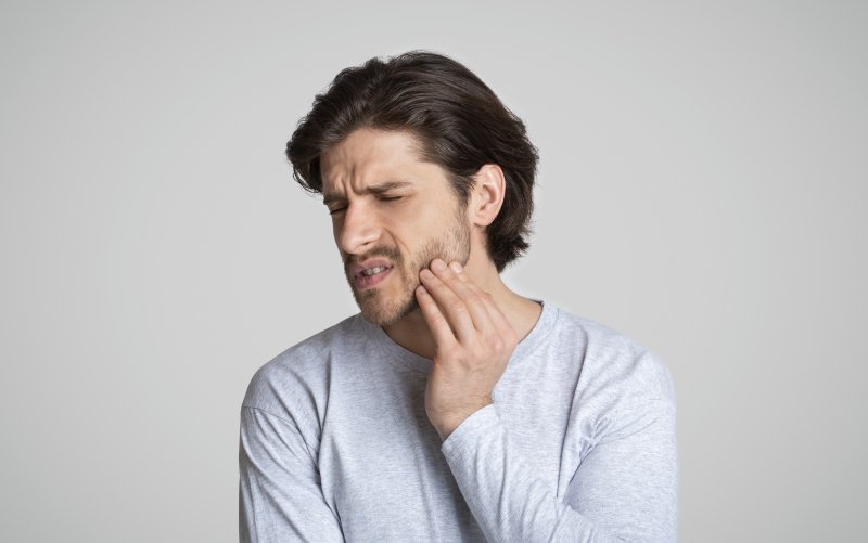 a young man holds his jaw in pain while experiencing a dental emergency