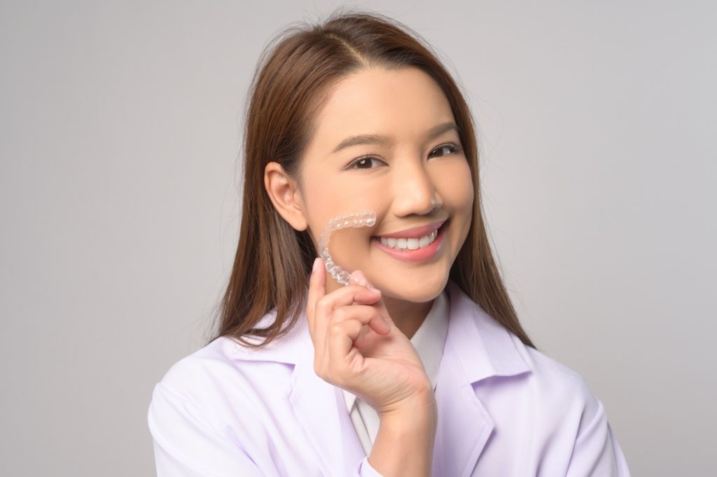 Woman smiling while holding Invisalign aligner