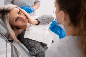 Woman holding side of face in pain in dentist's chair.