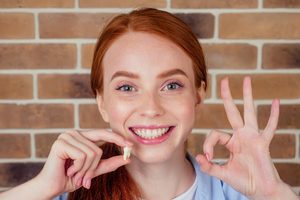 Woman holding extracted tooth in one hand and giving "ok" sign with the other